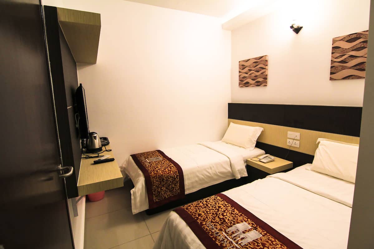 A hotel room with two beds, a desk with a telephone, and a wall-mounted light fixture.