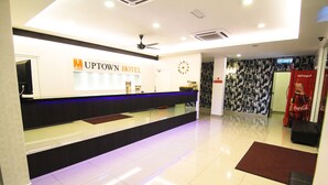 Ein Hotel-Empfangsbereich mit einer Rezeption, einer Uhr und einem an der Wand befestigten Schild für das Uptown Hotel.