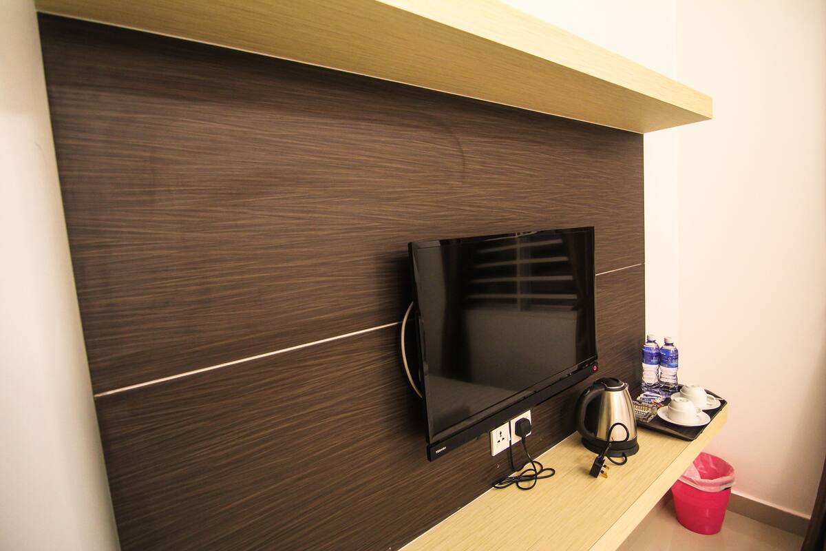 A wall-mounted television, a kettle, and a tray with cups and water bottles on a wooden shelf.