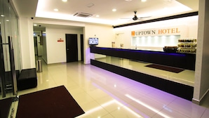 Ein Hotel-Rezeptionsbereich mit modernem Design, darunter ein Empfangsschalter, ein Fernseher und ein sichtbares Schild für das Uptown Hotel.
