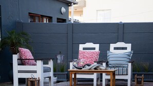 Zona junto a la piscina con sillones blancos y una mesa de madera.