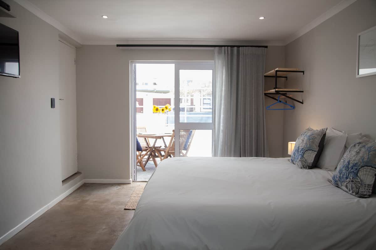 Quarto com uma cama grande, uma porta de correr de vidro para uma varanda e uma pequena mesa com cadeiras lá fora.