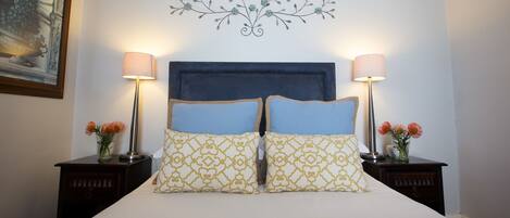 A neatly made bed with a blue headboard, two bedside tables with lamps, and a decorative wall piece above the bed.