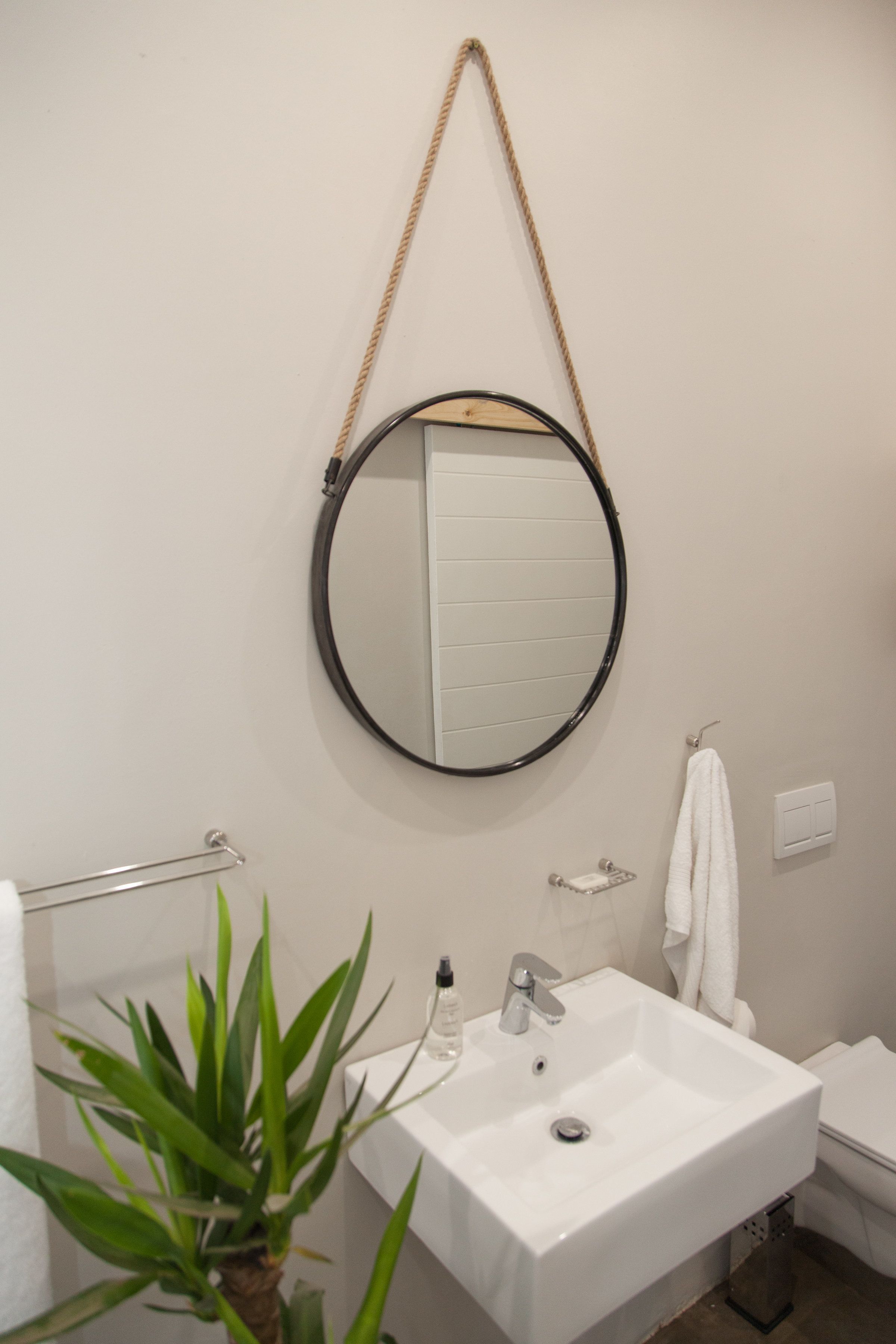 Ein Badezimmer mit einem weißen Waschbecken, einem runden Spiegel, einem Handtuchhalter und einem Blumentopf.
