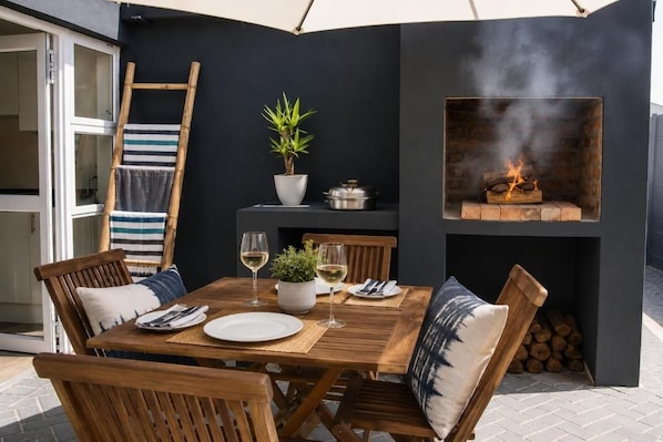 Un área de comedor al aire libre con una mesa dispuesta para dos personas, una chimenea y una planta en maceta.