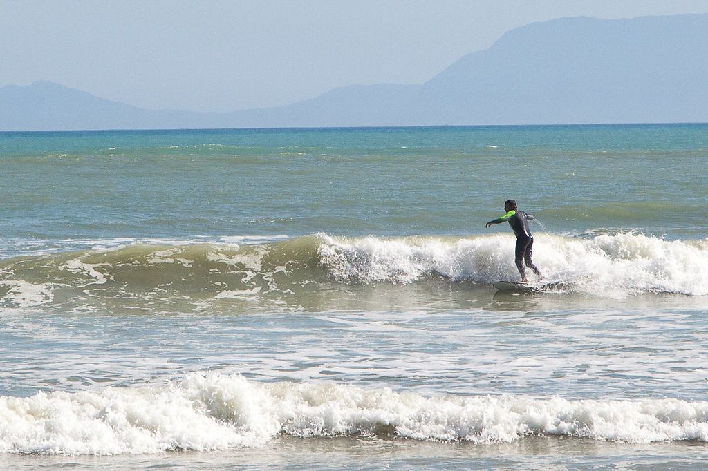 A person surfing on a wave in the ocean with mountains in the background.