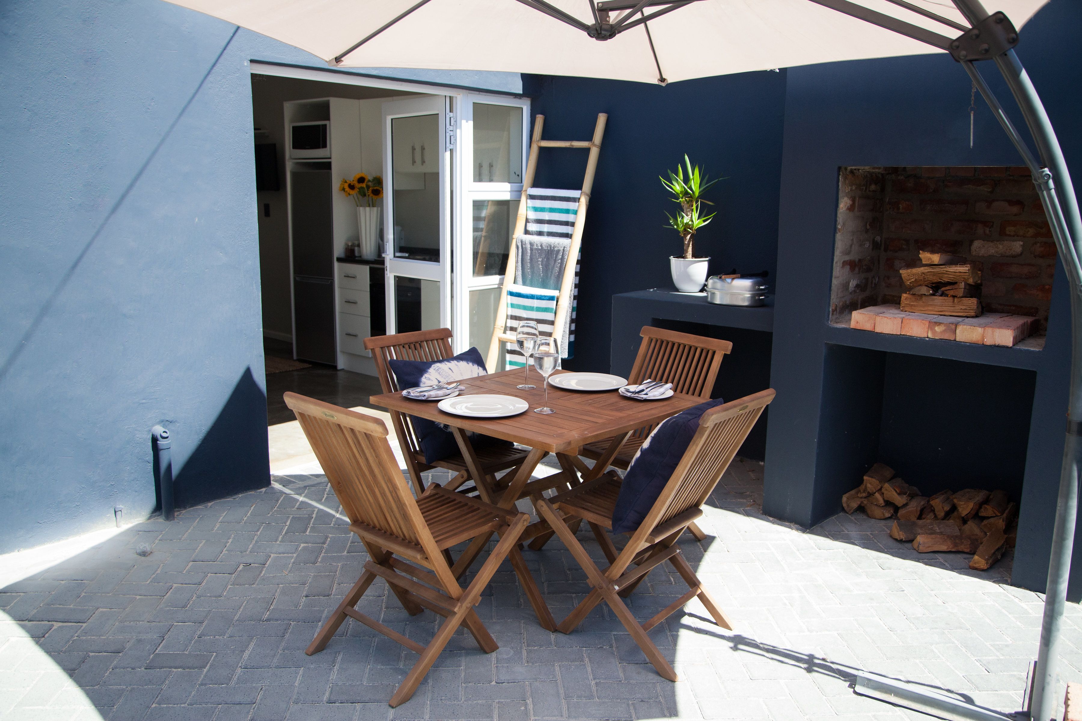 An outdoor patio with a wooden table and chairs, a brick fireplace, and a ladder leaning against the wall.