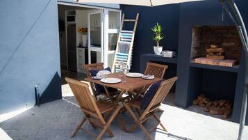 An outdoor patio with a wooden table and chairs, a brick fireplace, and a ladder leaning against the wall.