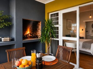A dining area with a fireplace, a table set for breakfast, and a view into the bedroom. - Loddeys Guesthouse (Cape Town)