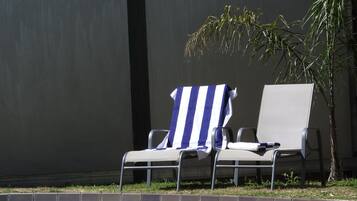 Área ao lado da piscina com duas espreguiçadeiras, uma delas com toalha listrada, e uma piscina.