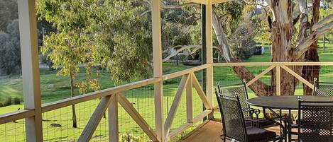 A covered outdoor area with a table and chairs, surrounded by a wooden fence and a view of a grassy landscape with trees.