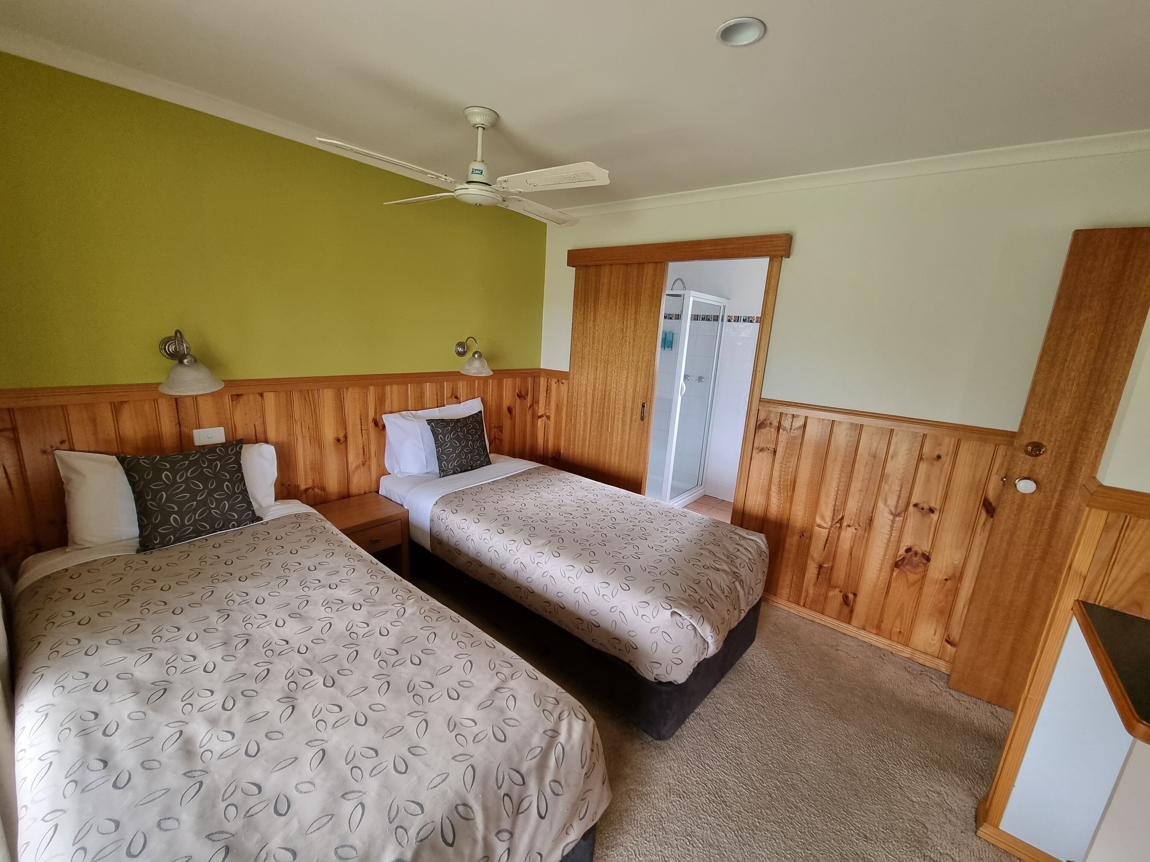 Ein Zimmer mit zwei Betten, einem Deckenventilator, einer Dusche und Holzvertäfelung.