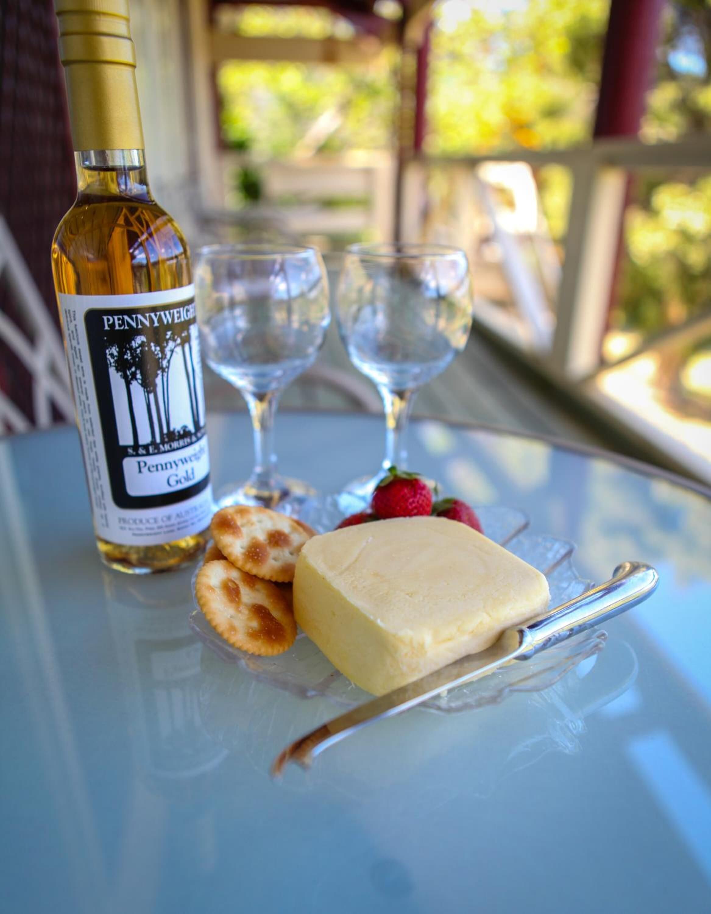 A bottle of Pennyweight Gold wine, two glasses, a piece of cheese, and some berries on a table.