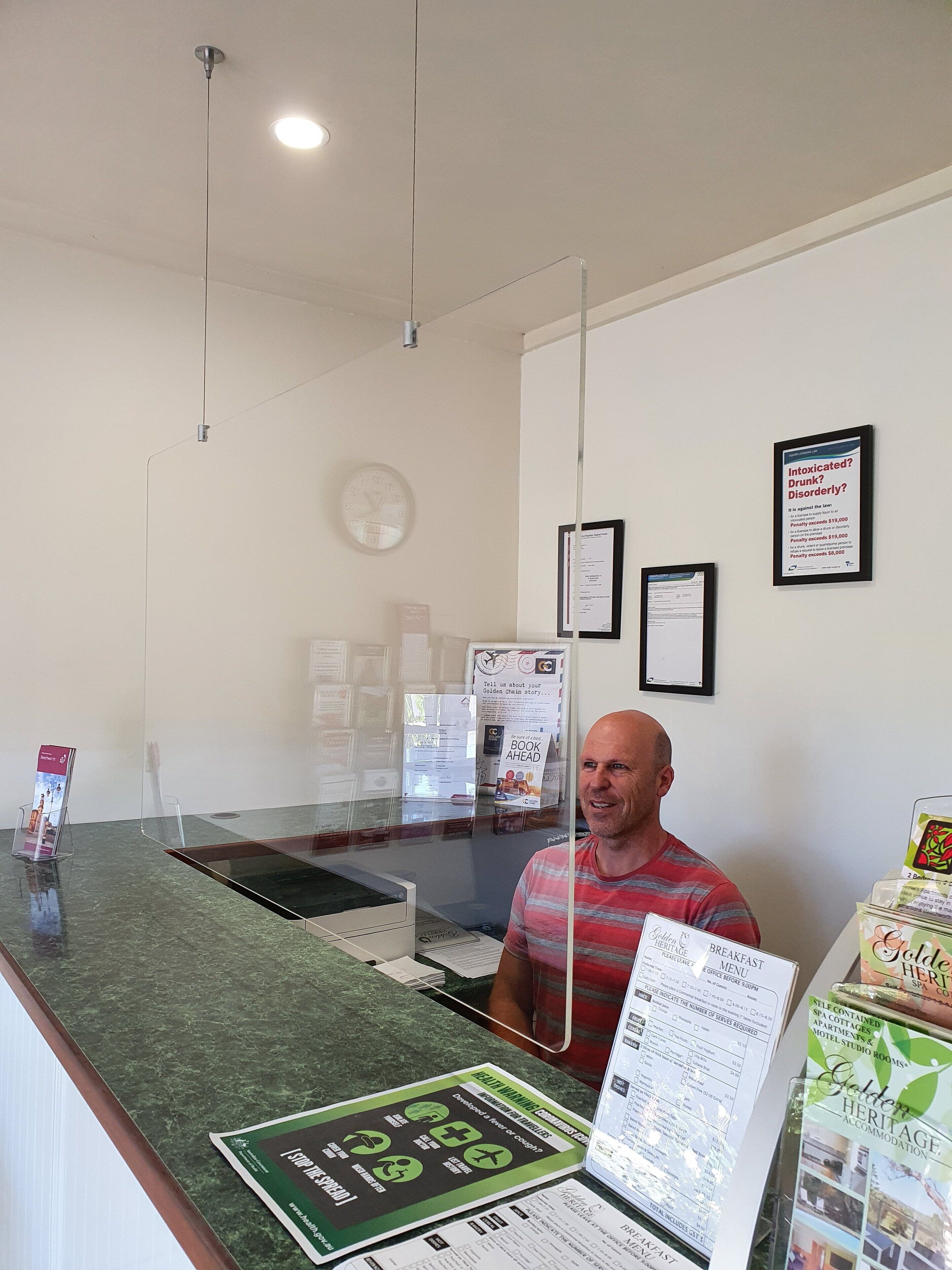 Una reception con un bancone dotato di divisorio in vetro, una sveglia e manifesti informativi appesi al muro.