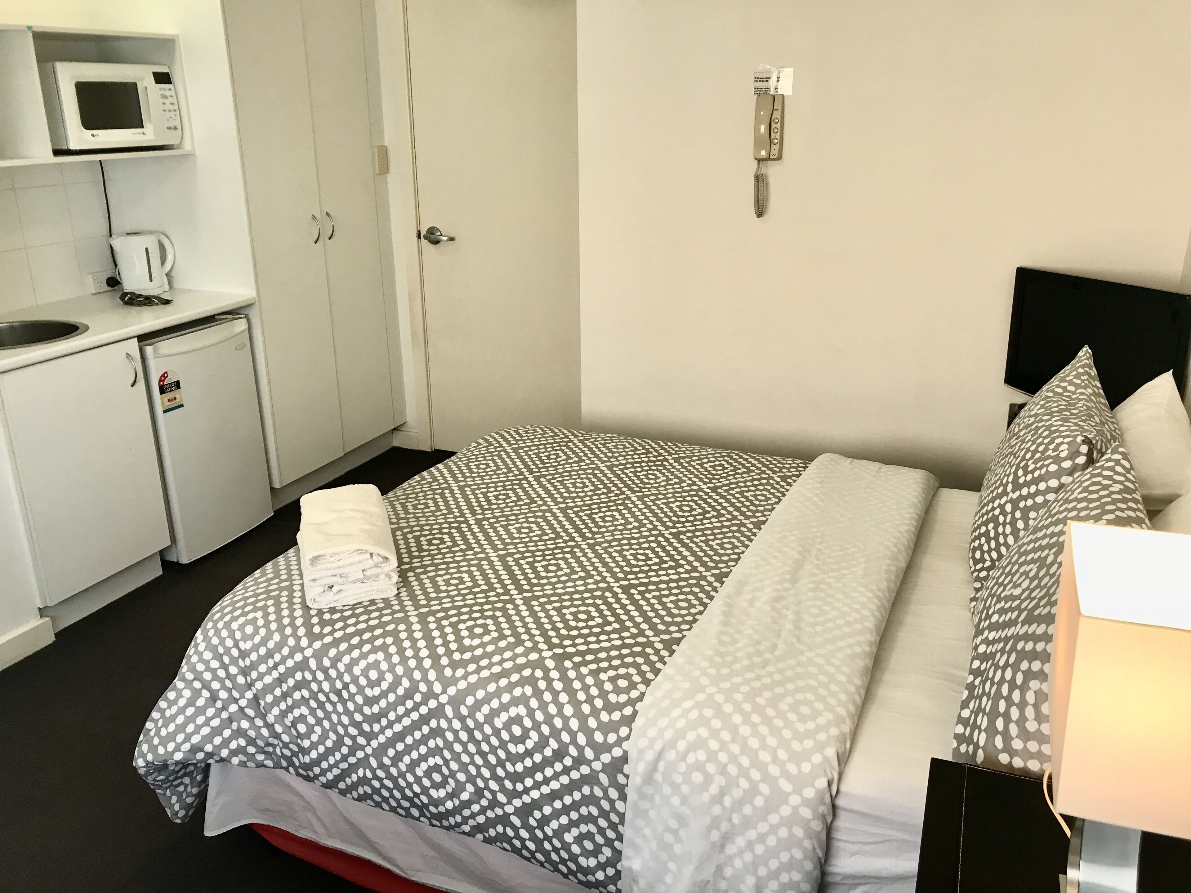 Habitació d'hotel amb llit, petita cuineta, microones, cafetera i televisió.