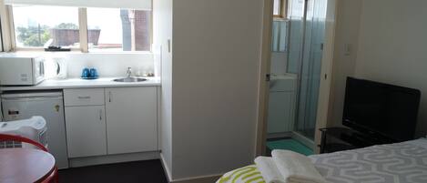 Habitación de hotel con kitchenette, una cama con colcha estampada, televisión y baño con cabina de ducha de vidrio.