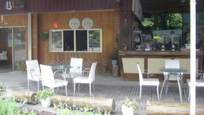 Un área de estar al aire libre con sillas y mesas blancas, una barra de madera con equipo de cocina y un letrero con caracteres chinos.