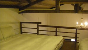 Una cama individual con cabecera de madera en una habitación con techo inclinado y una lámpara de araña.