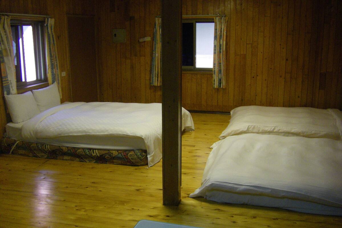 Una habitación con dos camas, suelo de madera y ventanas con cortinas.