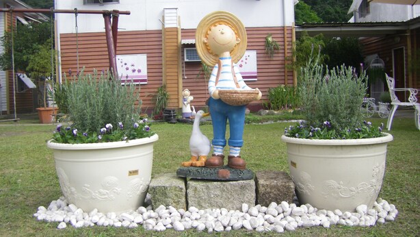 Un jardín con dos macetas grandes, una estatua de una persona con una cesta y una estatua de pato.