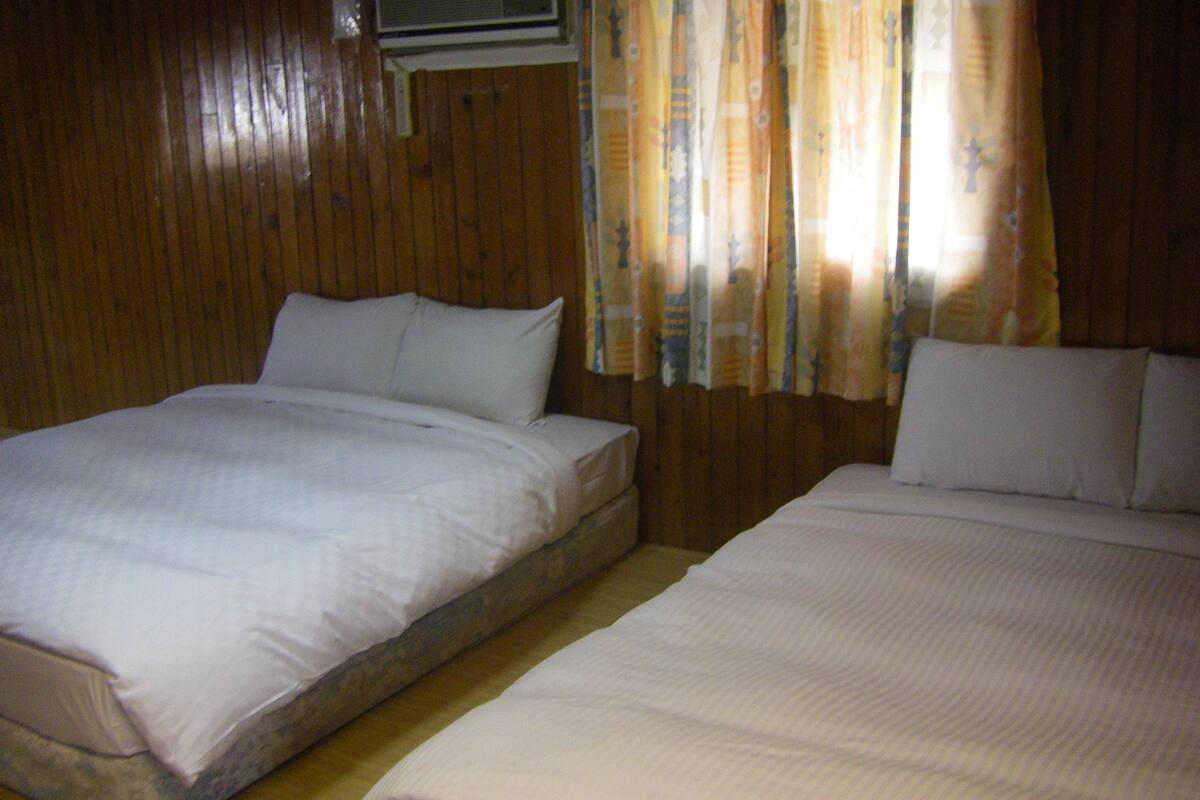 Una habitación con dos camas, paredes de madera y una ventana con cortinas.