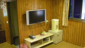Una habitación pequeña con paredes de madera, un televisor montado en la pared, un mueble bajo y un cubo de basura.