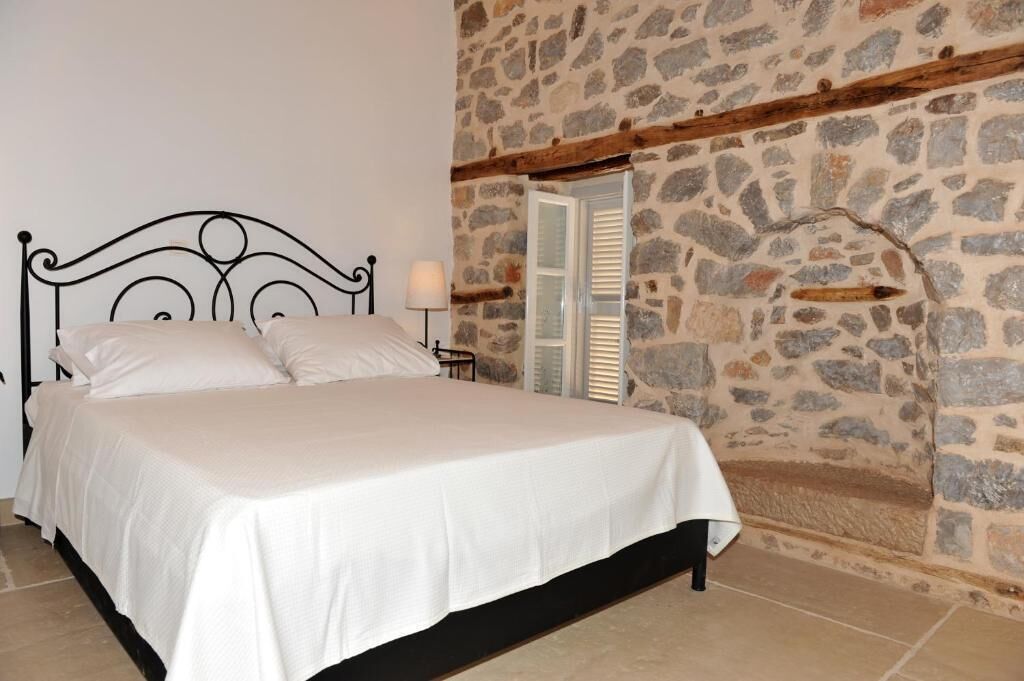 A bed with a headboard, a stone wall, and a window with shutters.
