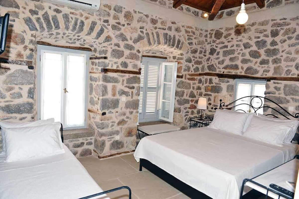 A bedroom with stone walls, two beds, a small table, and a lamp.