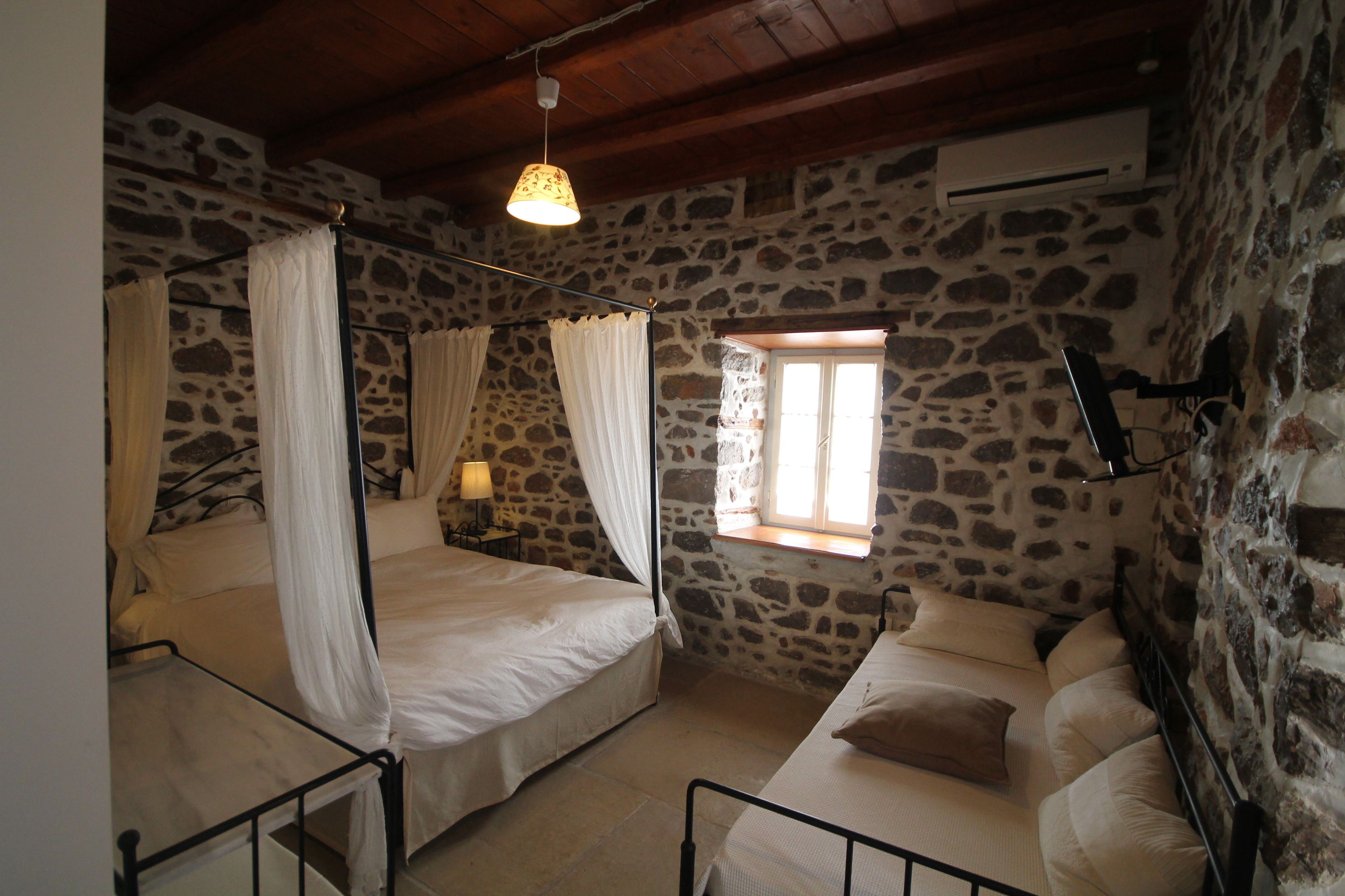 A room with two beds, stone walls, a window, and an air conditioning unit.