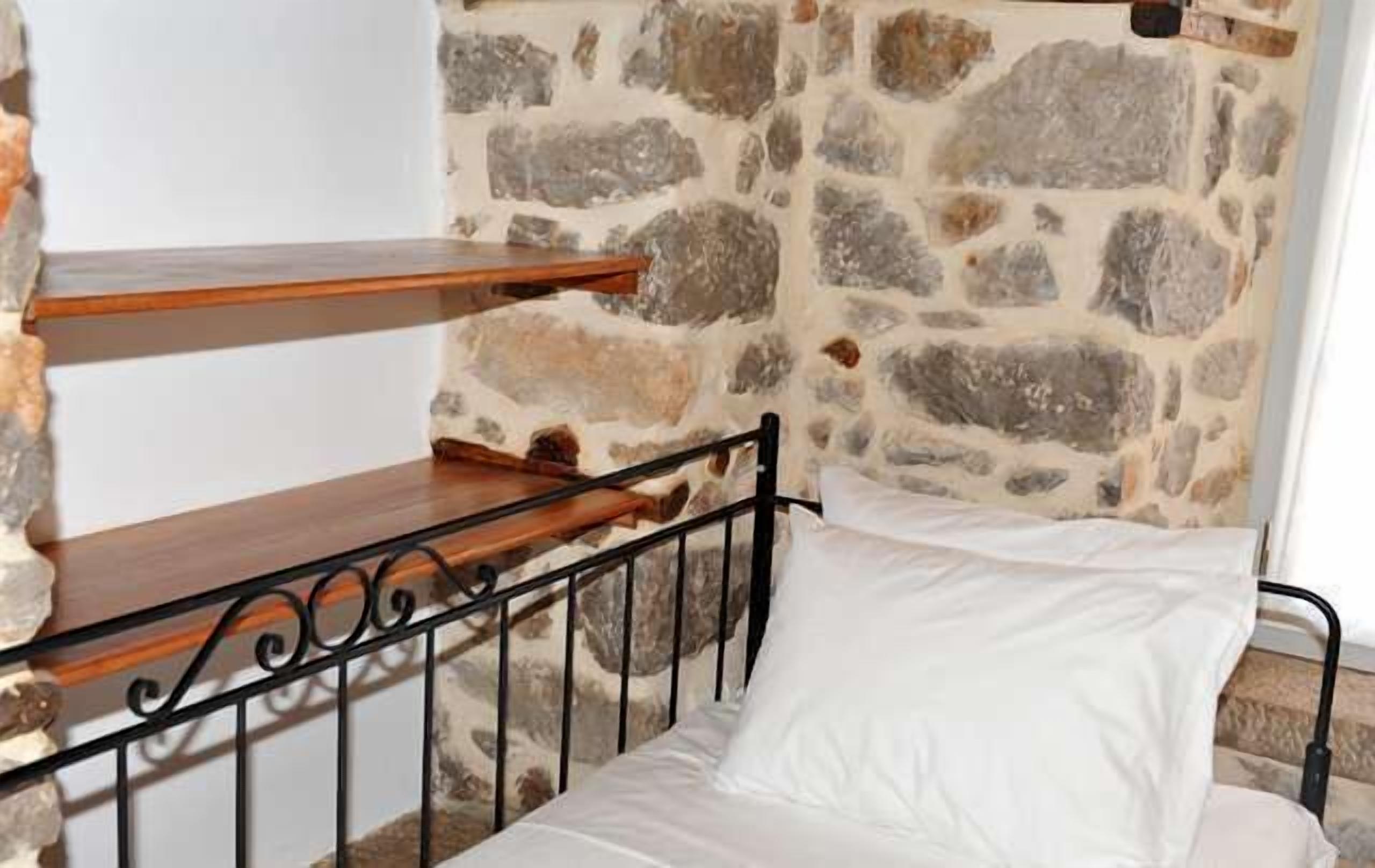 Een enkel bed met een wit kussen en een metalen frame, tegen een stenen muur.