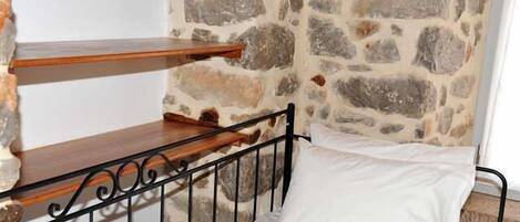 Een enkel bed met een wit kussen en een metalen frame, tegen een stenen muur.