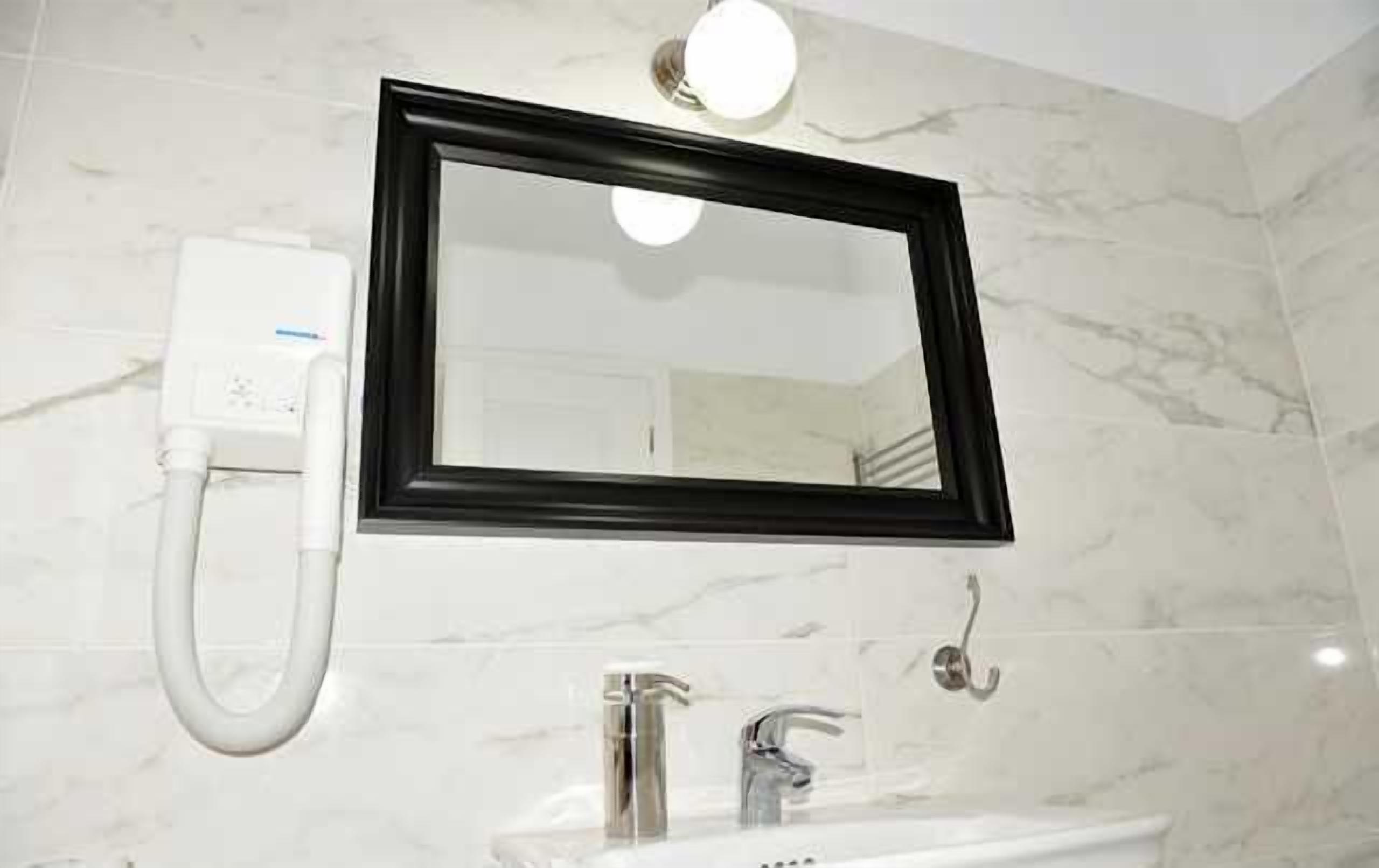 Un baño con lavamanos blanco, un espejo y un secador de manos.