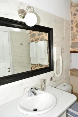 A bathroom with a white sink, a large mirror, and a towel rack. - Alexandra Guesthouse  (Hydra)