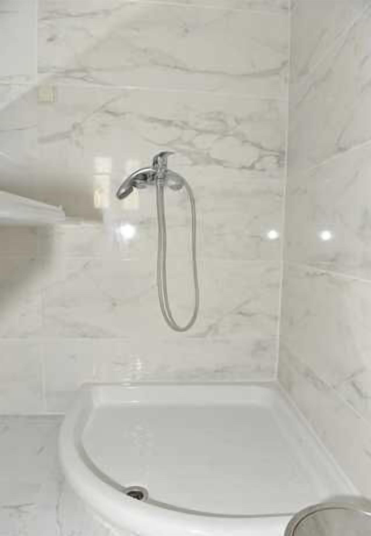 A bathroom with a white pedestal sink, a shower with a handheld showerhead, and marble walls.
