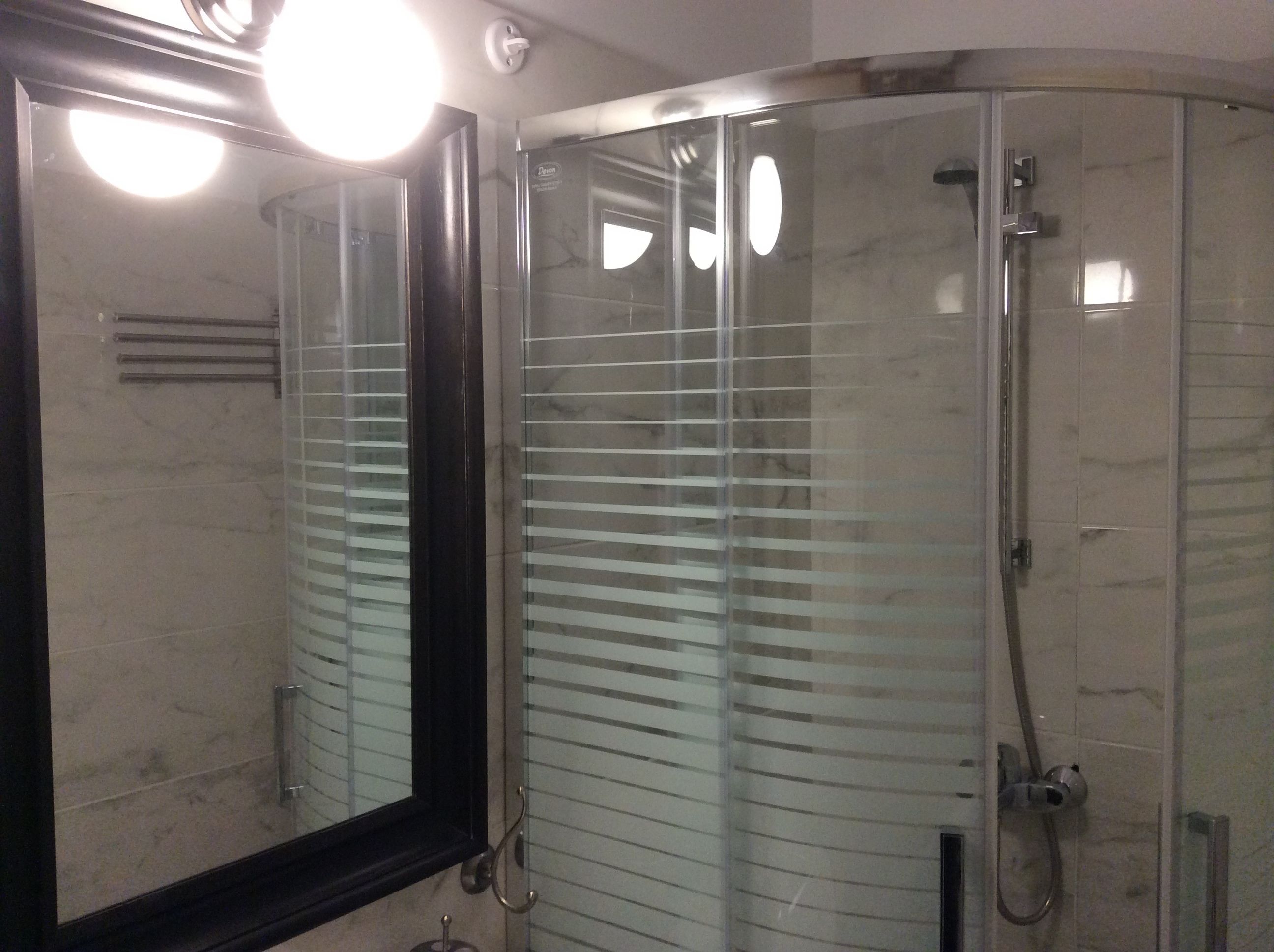 A modern bathroom with a glass shower enclosure, a large mirror, and a towel rack.