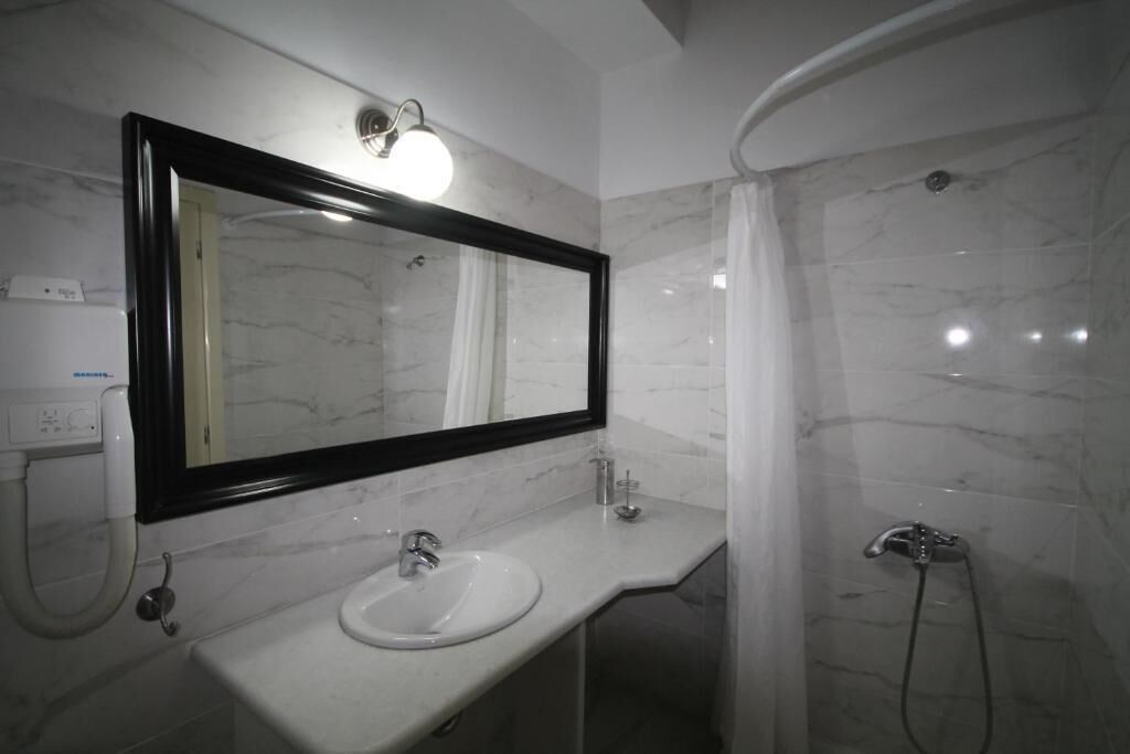 A bathroom with a white sink, a large mirror, and a shower area with a curved wall.