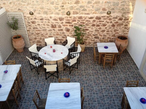 Une terrasse extérieure avec un sol en pierre, des tables rondes et carrées, des chaises et des plantes en pot.