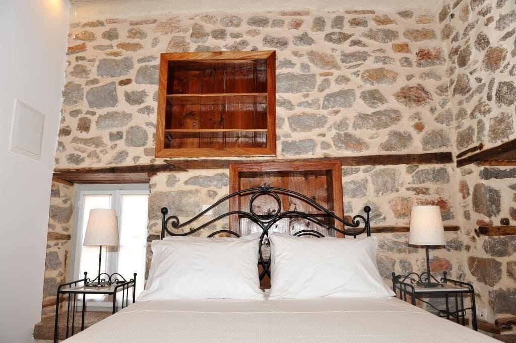 A bedroom with a stone wall, a wooden shelf, a metal bed frame, and two bedside lamps.