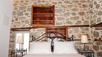 Un dormitorio con pared de piedra, estante de madera, estructura de cama metálica y dos lámparas de noche.