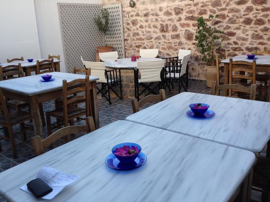 An outdoor dining area with stone walls and wooden furniture. Tables are set with blue bowls and white tablecloths.