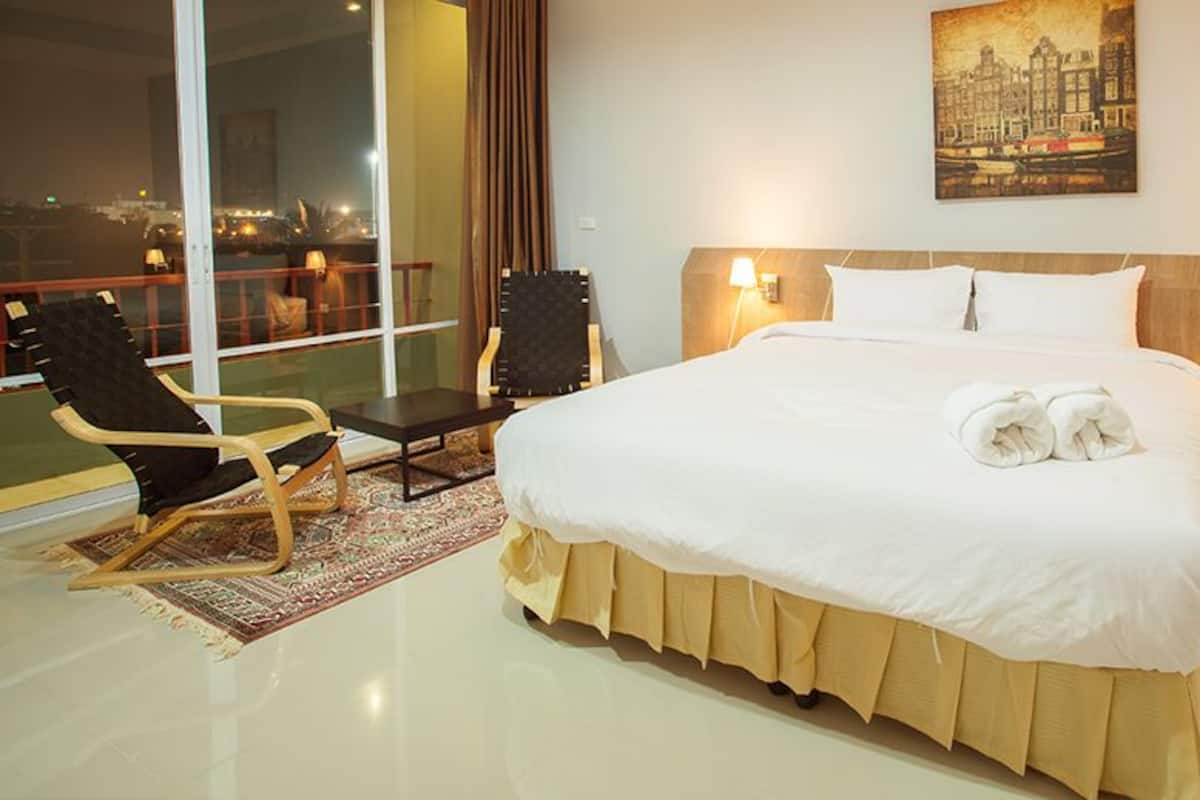 A hotel room with a large bed, two bedside lamps, a chair, a small table, and a view of the city at night.