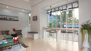 A modern living room with a glass coffee table, comfortable seating, a large window with a view, and a balcony with a railing. - Soontree House (Udon Thani)