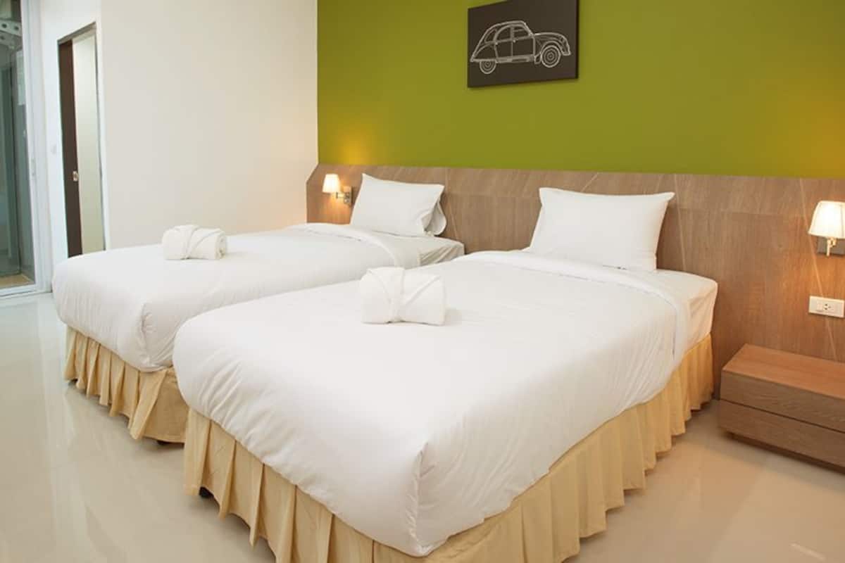 A hotel room with two beds, a wooden headboard, a glass shower, and a green accent wall.