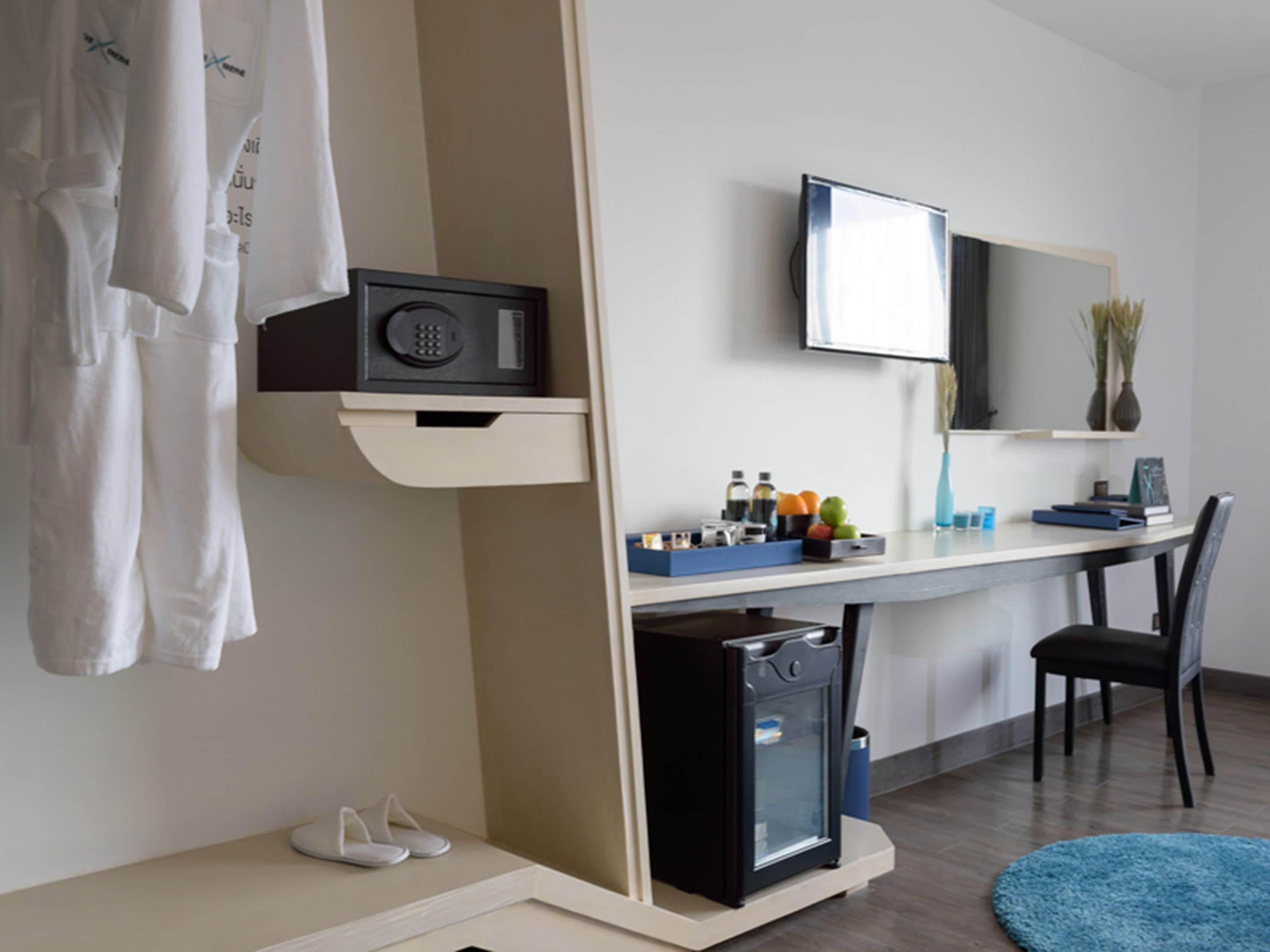 Ein modernes Hotelzimmer mit einem Bett, einem Schreibtisch mit Computer, einer kleinen Kühlschrank und einem Fernseher.