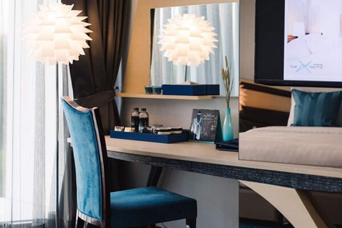 A hotel room with a bed, a desk with a chair, a television, and a window with curtains.