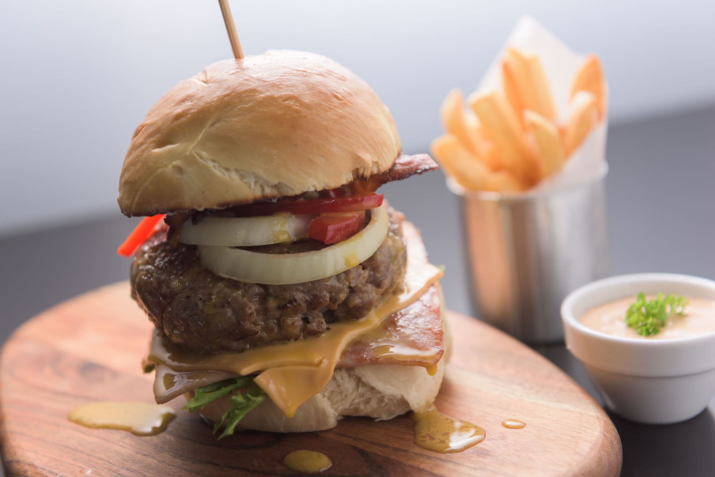 Un hamburger composé d’un pain, de laitue, de tomates, de fromage et d’une galette de viande, servi avec des frites et un petit bol de sauce.