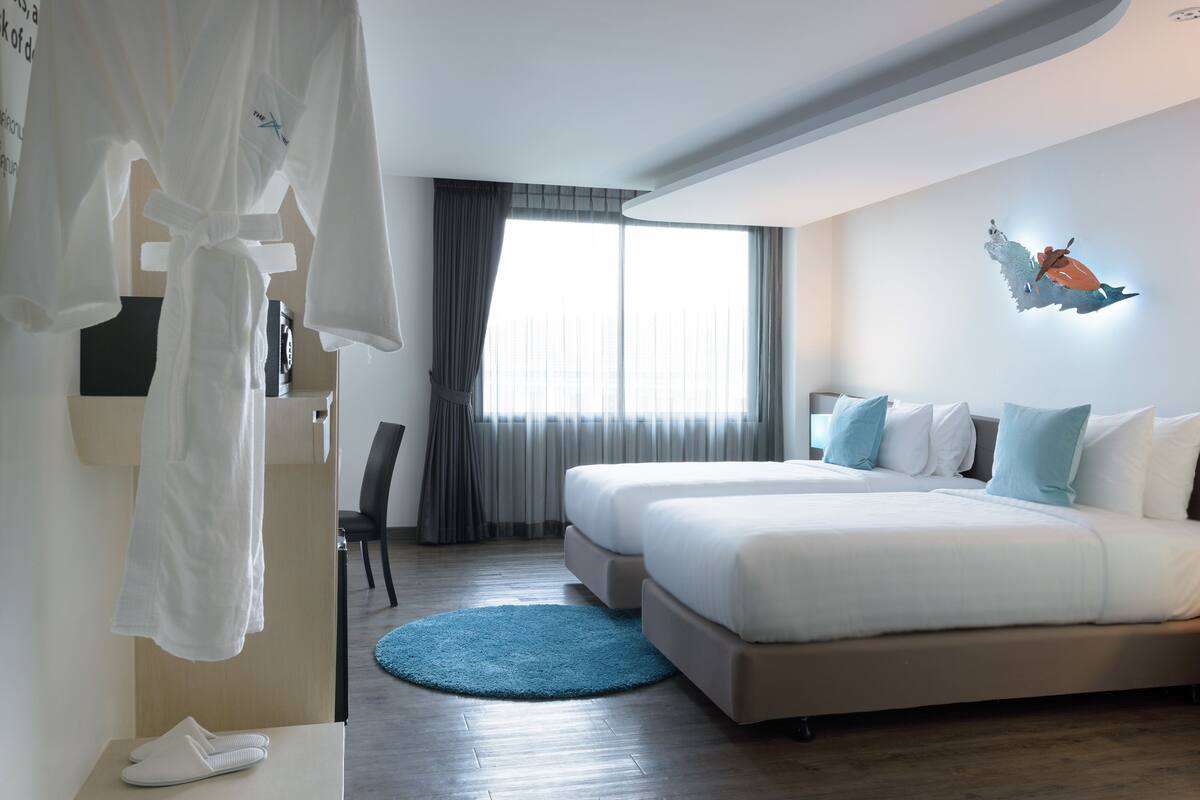 A hotel room with a large bed, a blue rug, a white robe, and a wall-mounted artwork.