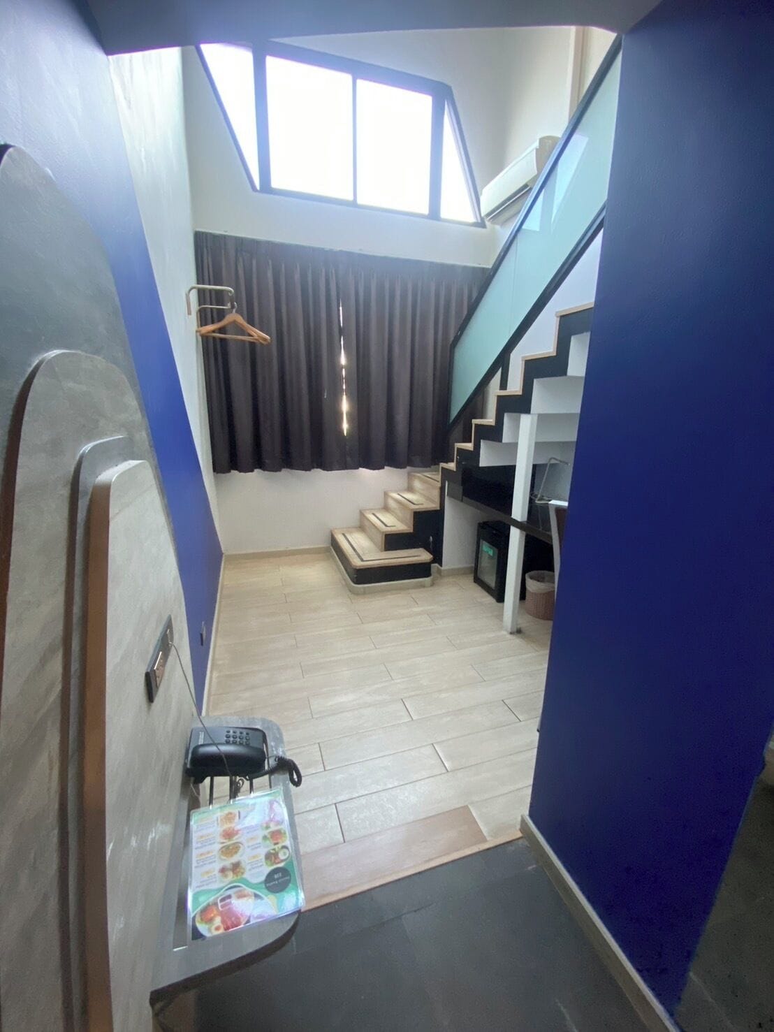 A compact living space with a staircase leading to an upper level, a small seating area, and a window with curtains.