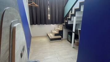 A compact living space with a staircase leading to an upper level, a small seating area, and a window with curtains.