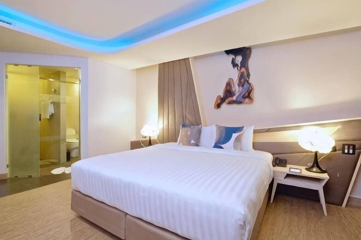 A hotel room with a large bed, bedside tables, a painting, and a door leading to a bathroom.